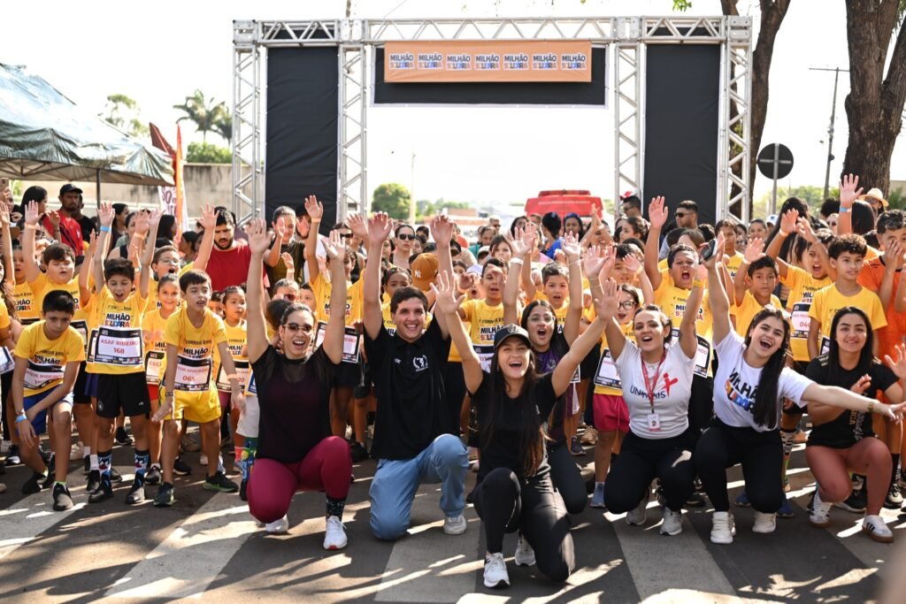 Crianças e equipe comemorando sob o pórtico de largada da Corrida Kids Milhão Solidária.