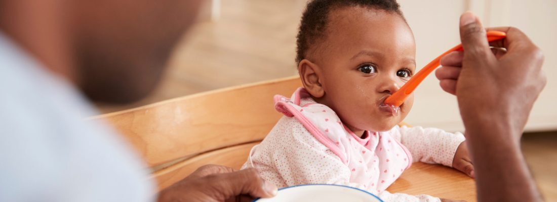 Father Feeding Baby Daughter In High Chair