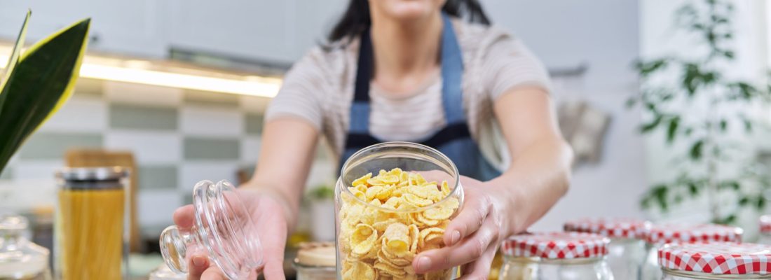 Woman showing a jar of corn flakes, food storage in the kitchen. The female tells about the organization of the pantry, about cooking